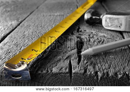 A low angle image of a yellow tape measure, hammer, and pencil on a wooden workbench - selective colour.