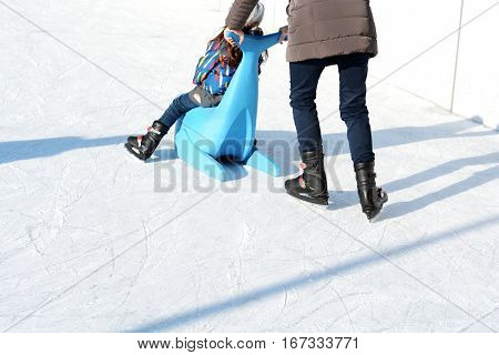 Family fun on outdoor ice rink, kid learning to skate with plastic seal as training aids