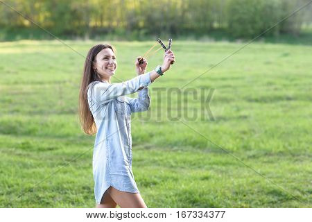 Woman using a slingshot. Over meadow background