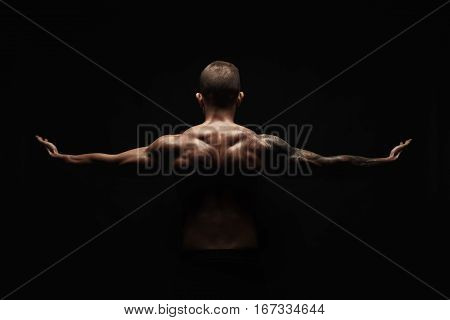 Unrecognizable man bodybuilder shows strong hands and neck muscles, athletic trapezius. Low key, studio shot on black background.