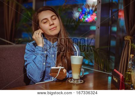 Music smartphone in female hand, on cafe interior background, injoy
