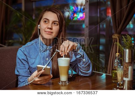 Music smartphone in female hand, on cafe interior background, injoy