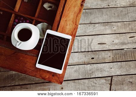 Cup of morning tea or coffee and tablet with blank screen on the wooden table over porch deck. Top view.
