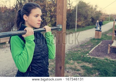Attractive brunette doing pullups in park. Outdoor fitness.