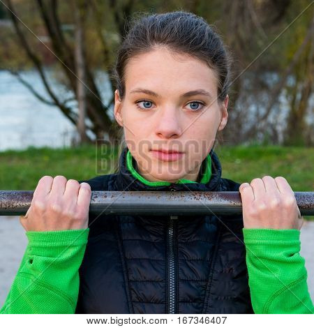 Attractive brunette doing pullups in park. Outdoor fitness.