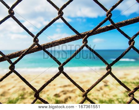 Closeup photo of a rusty old chain link fence with a beach in the background near Makaha Hawaii.