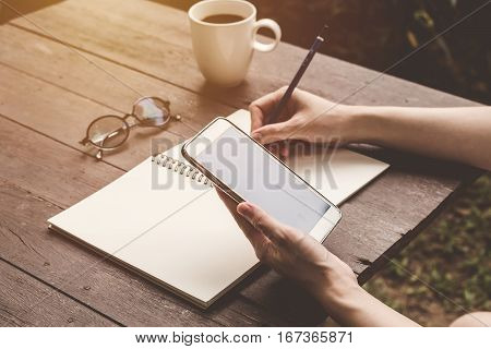 Close Up Hand Woman Writing Notebook And Holding Phone On Wood Table Backhround With Vintage Toned.