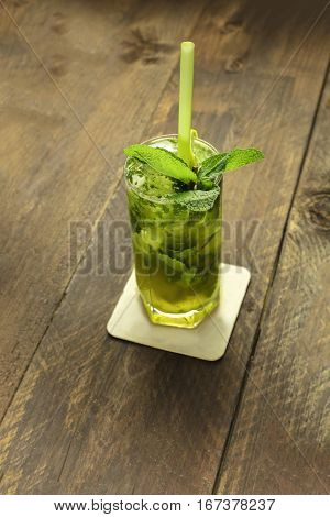 A photo of a mojito cocktail with mint leaves and a drinking straw, on a dark wooden background with copyspace