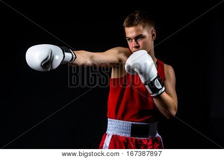 Young handsome boxer sportsman in red boxer suit and white gloves standing on black backgound. Copy space.