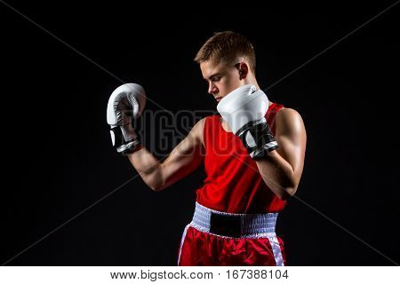 Young handsome boxer sportsman in red boxer suit and white gloves standing on black backgound. Copy space.