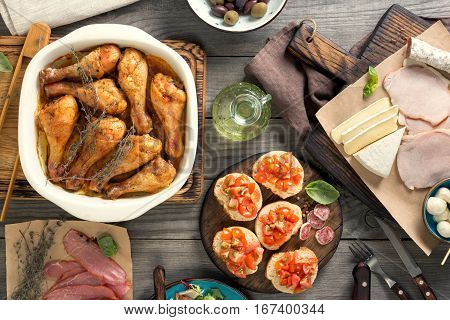 Baked chicken legs with variety of snacks on the wooden table. Italian food table dinner table concept