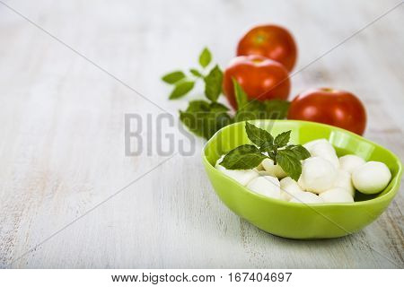 Mozzarella in a green plate on a wooden table. Mozzarella balls with basil leaves and tomato on a wooden board. Ingredients for caprese salad.