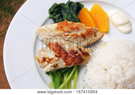 Indigenous Fijian seafood and vegetables dish served in a plate. Fried fish with papaya rice and steamed pumpkin leaves.