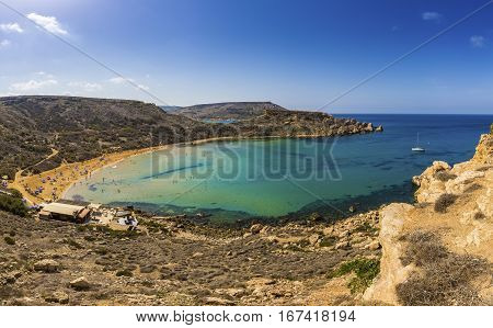 Ghajn Tuffieha Malta - Beautiful summer day at Ghajn Tuffieha sandy beach with sail boat blue sky and crystal clear green sea water