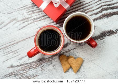 two red coffee cup, hearts cokies and gift box on wooden surface. Valentines day concept.