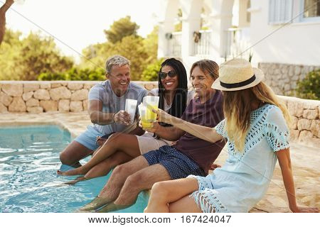 Two couples make a toast with legs dipping in swimming pool