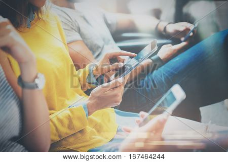 Group of young hipsters sitting on sofa holding en hands and using digital tablet, smartphone.Coworking team concept.Horizontal, blurred background