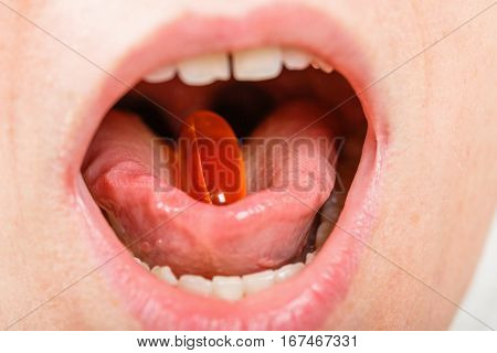 Close up photo of young woman with fish oil capsule in her mouth