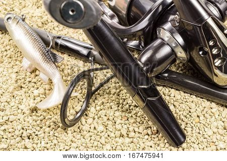 Spinning silicone fish and fishing reel on the background of rocky ground