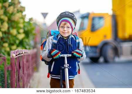 Active school kid boy in safety helmet riding with his scooter in the city. Happy child in colorful clothes biking on way to school. Safe way for kids outdoors to school.