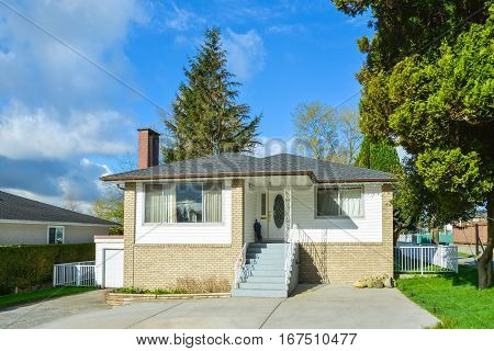 Modest family house with garage in Canada. Residential house with concrete paved front yard on blue sky background