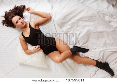 Sexy lazy girl in black body hugging a pillow on the bed. Young attractive woman lying lazing in bedroom at morning.