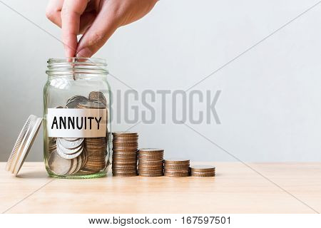 Hand putting coin in jar word annuity with money stack Concept business finance and investment