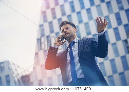 Low angle view of business man gesturing while speaking on mobile phone against office building
