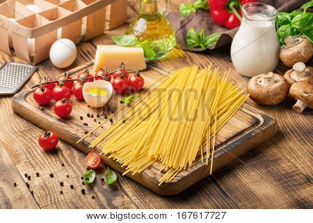 Raw Italian spaghetti with different ingredients for cooking Italian pasta on a wooden board on wooden table