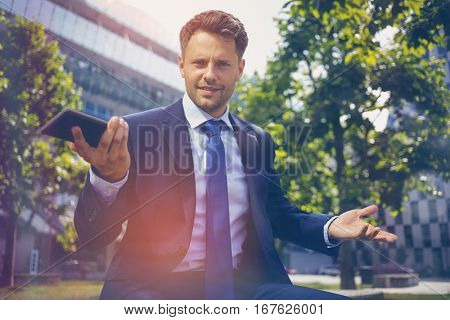 Portrait of confused businessman holding mobile phone outside office