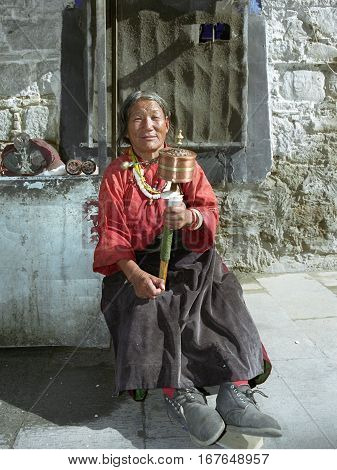 Lhasa, Tibet, China - September 2007: An elderly Tibetan pilgrim lady in big boots with prayer wheel on September 2007 in Lhasa, Tibet, China.