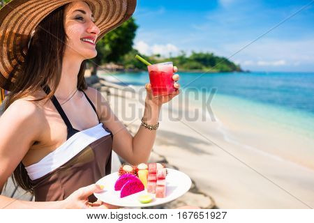 woman tourist at tropical beach eating fruit like water melon, pineapple and barbary fig for breakfast