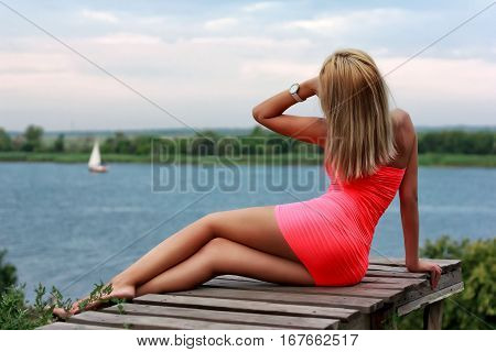Beauty sexy girl on the wooden jetty looking to the sailing yacht in the river