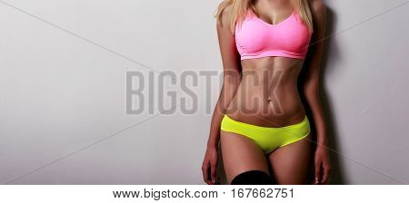 Beautiful sporty female body in pink and green bikini isolated on gray background