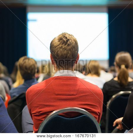 Business and entrepreneurship symposium. Speaker giving a talk at business meeting. Audience in the conference hall. Rear view of unrecognized participant in audience.