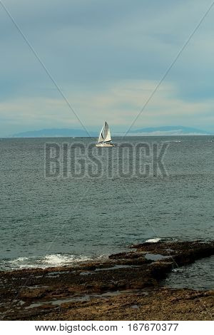 Beautiful sailing ship or yacht boat with white sails in calm blue sea water floats inshore outdoors on sunny summer day on sky background
