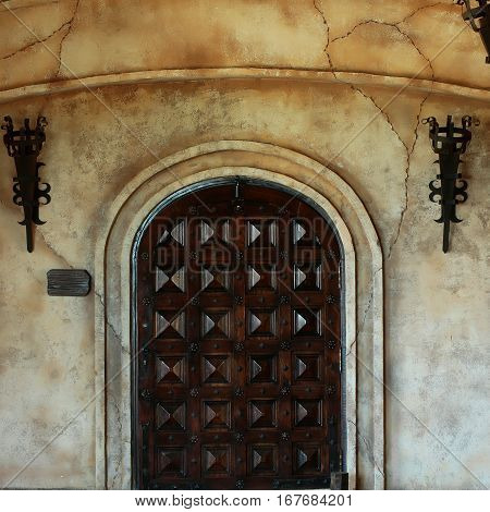 Old wooden arch door medieval style portal in dark brown color on stone building on cracked cement wall background