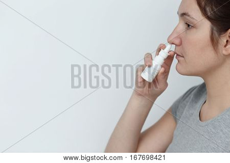 Young woman using nose drops isolated on white background. Portrait of a girl with a nasal spray in hands. The concept of treatment for allergies or the common cold.