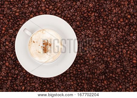A white cup of cappuccino on coffee beans background