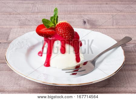 panna cotta dessert with strawberry sirup and mint leaf on light wooden background