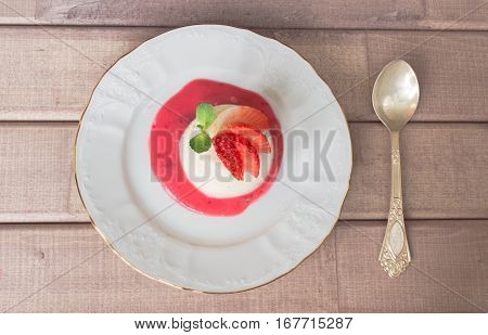 panna cotta dessert with strawberry sirup and mint leaf with spoon on light wooden background