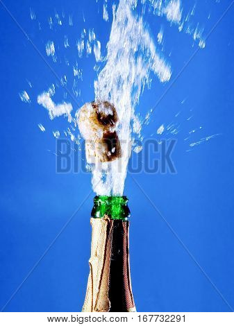 Bottle of champagne with a popping cork (against a bright blue background)