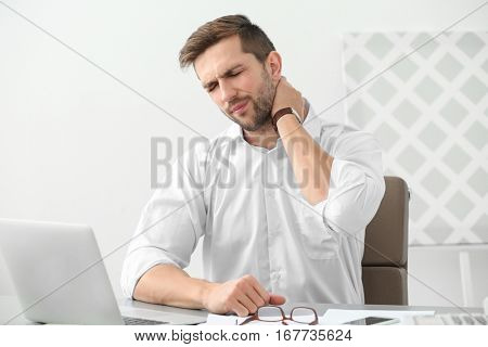 Handsome man suffering from neck pain in office
