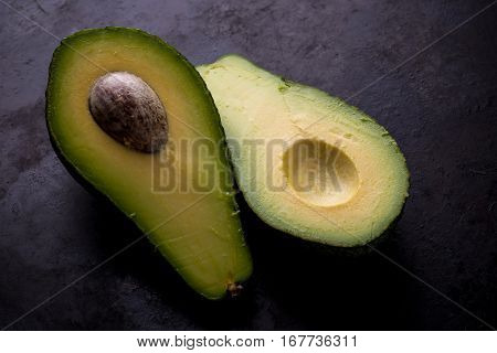 Single Avocado Severed In Half On Worn Black Tray