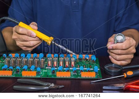 Technician holds soldering iron and solder to do board repairing