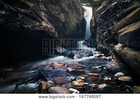 Landscape with waterfall flowing into a stony brook.