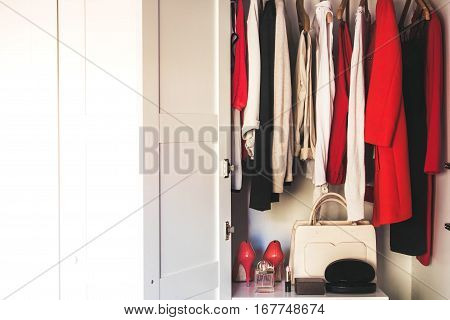 White wardrobe with hanging women's clothing and women's accessories on the shelf