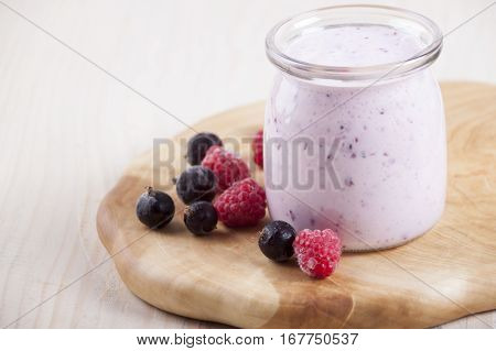 Smoothies with frozen berries black currants and raspberries in jar on a wooden stand.
