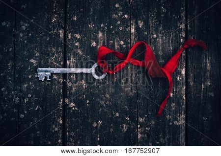 an antique rusty key on red ribbon on vintage wooden board