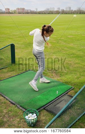 Girl with cammock hits ball on green golf course at spring day